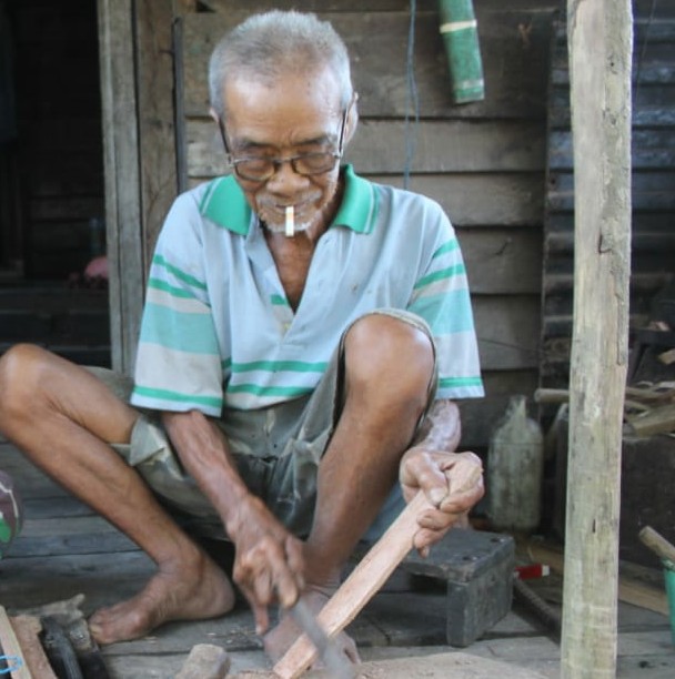 TERINGAT ANGGOTA SATGAS TMMD REG KE 108 KODIM 1203/KTP MEMBANTU MEMBUAT SARUNG PARANG DARI KAYU